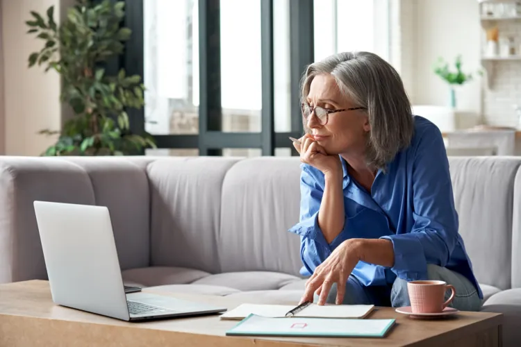 Woman reading laptop with paperwork