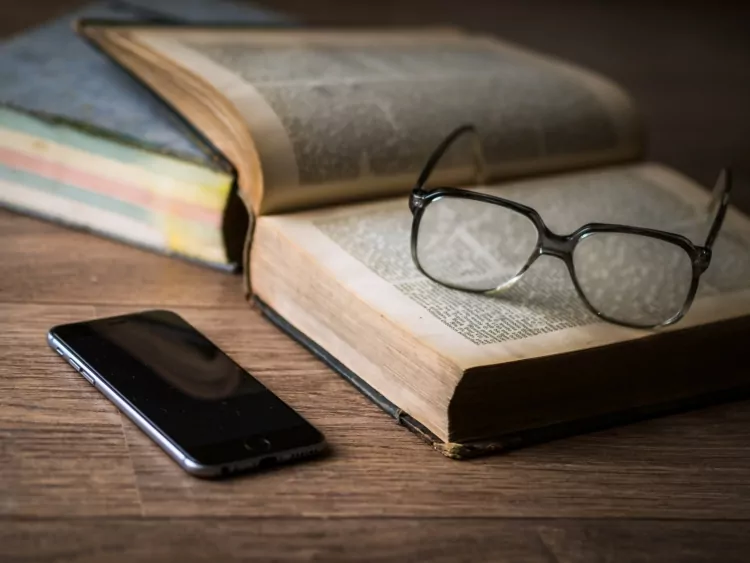 Glasses resting on an open book next to a phone